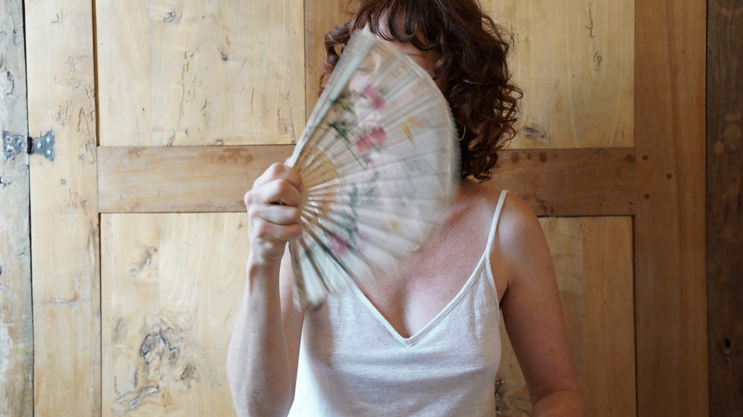 Portrait d'une femme avec un éventail en été, évoquant la ménopause et le bien-être corporel